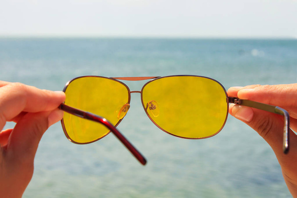 Κίτρινα γυαλιά ηλίου στο θαλασσινό νερό και μπλε φόντο του ουρανού. Ηλιόλουστη μέρα, καλές διακοπές, καλή ξεκούραση, ευτυχία. - Φωτογραφία, εικόνα