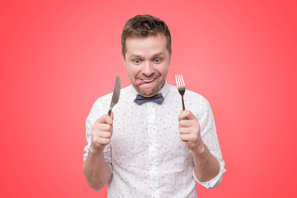 Uomo che tiene forchetta e coltello a portata di mano pronto da mangiare, leccare le labbra
 - Foto, immagini