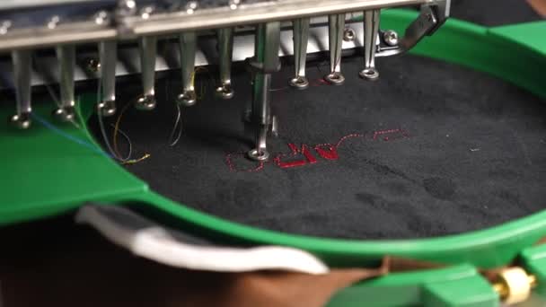 黒い布に赤い糸が付いた自動機械刺繍パターン。ロボティクスは、生産ラインの調整に取り組んでいます。ロボットミシン。自動ミシン。コンピュータコントロールミシン - 映像、動画