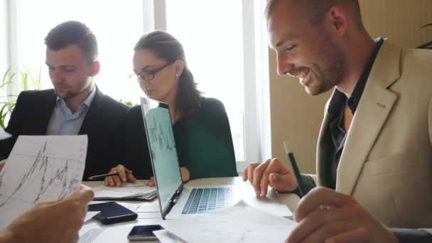 Young coworkers discussing income graphs during team meeting. Business people sitting at the table and planning strategy for corporate project. Business team analyzing financial reports in office - Кадры, видео