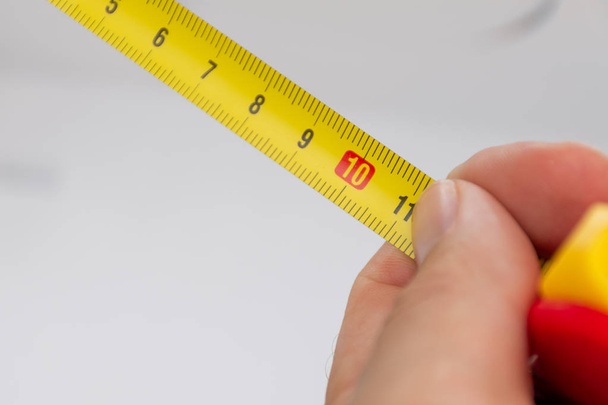 Un primer plano de una cinta métrica amarilla medida con una mano blanca hol
 - Foto, Imagen