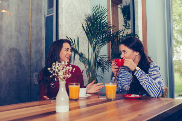 Happy female friends talking and drinking coffee while looking e - Foto, Imagem