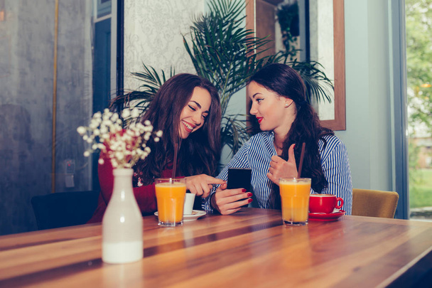 Δύο ενθουσιασμένοι νεαρά κορίτσια που χρησιμοποιούν το κινητό τηλέφωνο ενώ κάθονται στο καφέ - Φωτογραφία, εικόνα
