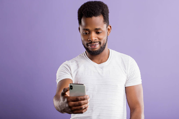 Young happy african man with cellphone isolated on lilac background - Фото, изображение