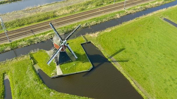 Veduta aerea di un vecchio mulino a vento tradizionale olandese sulla campagna rurale nei Paesi Bassi con una diga, canali. Ferrovia. ponte e una strada
. - Foto, immagini