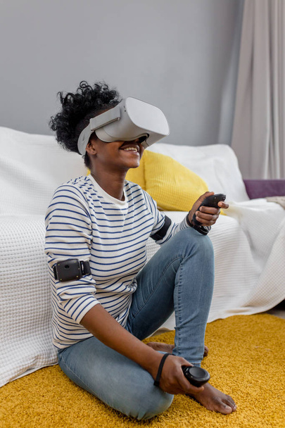 African woman watching video using VR glasses with remote control at home. - Фото, изображение