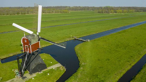 Veduta aerea di un vecchio mulino a vento tradizionale olandese sulla campagna rurale nei Paesi Bassi con una diga, canali. Ferrovia. ponte e una strada
. - Foto, immagini