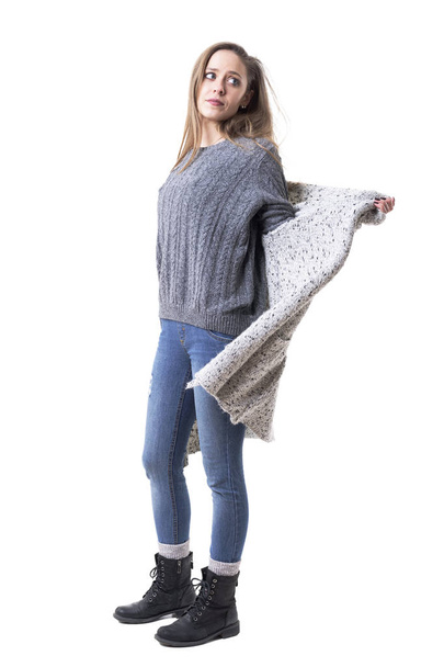 Side view of young stylish woman in winter clothes undressing taking off knitted cardigan. Full body isolated on white background.  - Фото, изображение