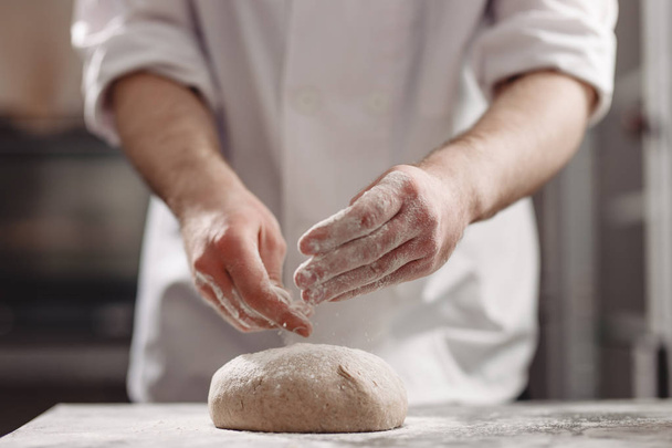 Baker  kneads  dough on the table in the bakery - Fotoğraf, Görsel