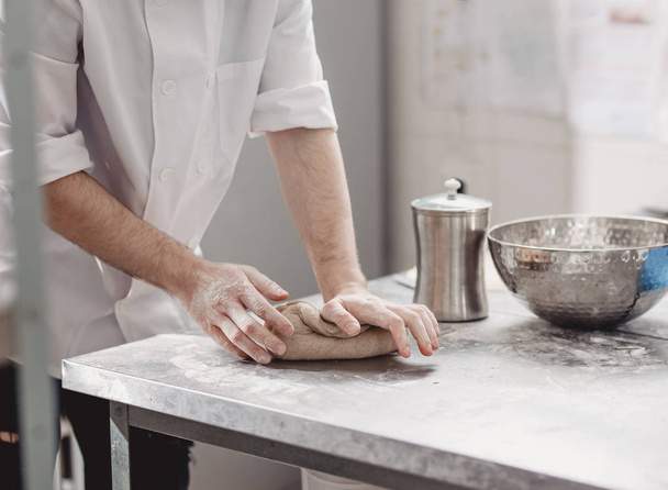 Baker  kneads  dough on the table in the bakery - 写真・画像