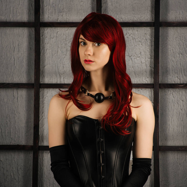 Portrait of Red-haired girl in a leather corset with gag ball - Photo, Image