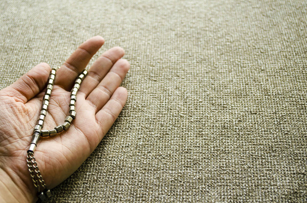 Light ivory rosary in the open female palm. The hand of a young woman holds a rosary in prayer. Background copy space. Selective focus image. - Zdjęcie, obraz