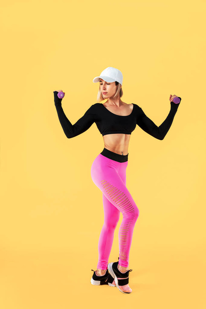 Sporty woman in fashionable sportswear does the exercises with dumbbells. Photo of muscular woman on yellow background. - Foto, Bild