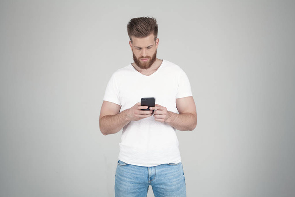 Portrait d'un bel homme barbu sexy. il écrit des SMS à ses amis ou sa petite amie. il se tient devant le fond blanc
 - Photo, image