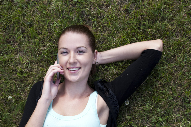 Young woman lying on the grass with phone in hand - Valokuva, kuva