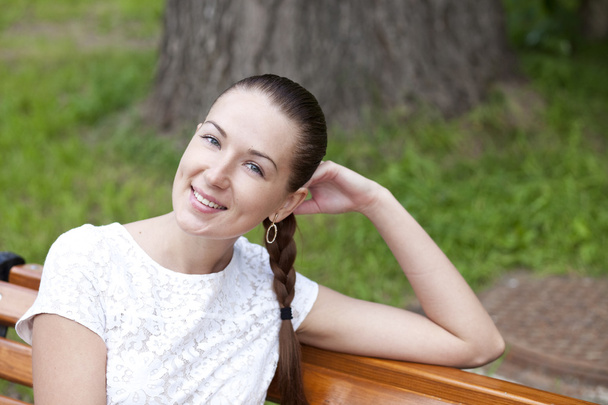 Brunette sitting on a bench in a summer park - Photo, Image