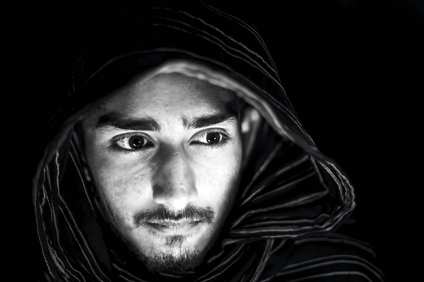 Portraitaufnahme eines Mannes in schwarz-weißer Farbe isoliert auf schwarz, die Wut im Gesicht ausdrückend und mit schwarzem Tuch im Gesicht. - Foto, Bild