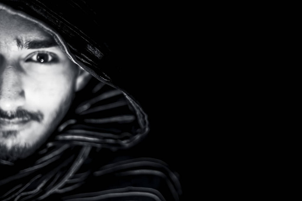 Retrato del hombre en color blanco y negro aislado en negro expresando enojo en su cara y vistiendo tela de color negro en su cara
. - Foto, Imagen