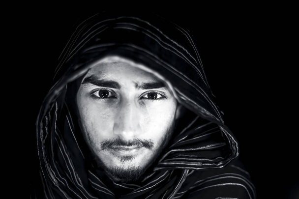 Retrato del hombre en color blanco y negro aislado en negro expresando enojo en su cara y vistiendo tela de color negro en su cara
. - Foto, Imagen