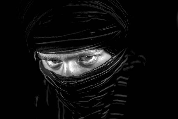 Opvallend portret van mannelijke tiener geïsoleerd op zwart met piercing expressieve ogen samen met een doek bedekken gezicht behalve ogen. Moed en blonditeit uiten. - Foto, afbeelding