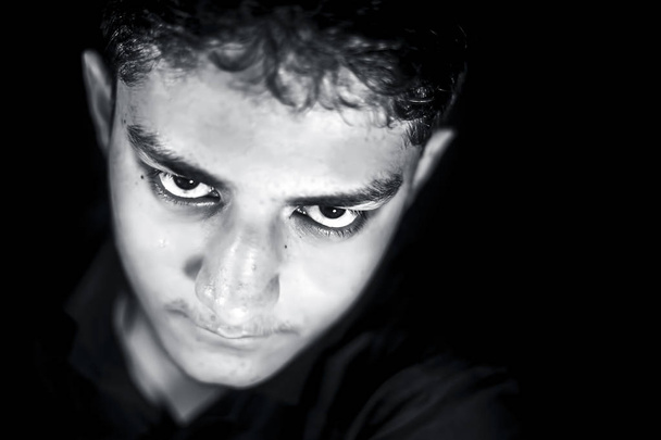 Portrait shot of young white isolated on black wearing black colored shirt and expressing angriness and mysteriousness on his face. - Photo, image