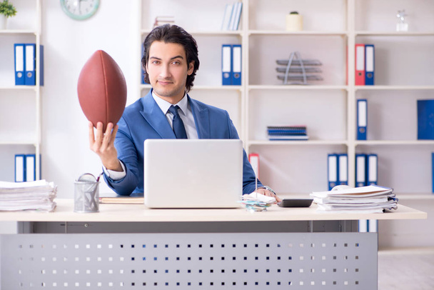 Jonge knappe zakenman met een rugbybal in het kantoor - Foto, afbeelding