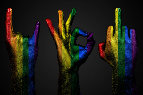 un ensemble de trois mains avec un drapeau peint LGBT montrer majeur doigt, chèvre et Ok, un signe d'agression, de protestation et d'approbation sur un fond sombre
. - Photo, image