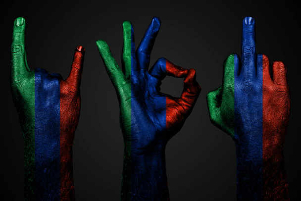 un conjunto de tres manos con una bandera pintada Daguestán mostrar el dedo medio, cabra y bien, un signo de agresión, protesta y aprobación sobre un fondo oscuro
. - Foto, Imagen
