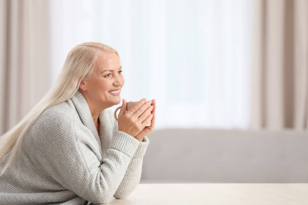 Ritratto di bella donna anziana con tazza di tè seduta a tavola al chiuso. Spazio per testo
 - Foto, immagini