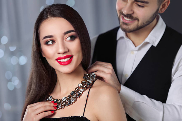 Man putting jewelry on beautiful young woman against blurred lights - Valokuva, kuva