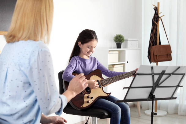 Little girl playing guitar with her teacher at music lesson. Learning notes - 写真・画像