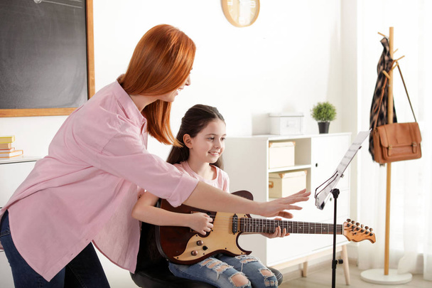 Little girl playing guitar with her teacher at music lesson. Learning notes - Photo, image