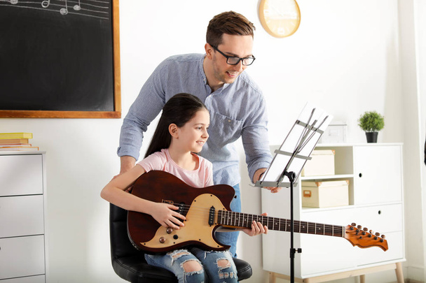 Little girl playing guitar with her teacher at music lesson. Learning notes - Foto, Imagen