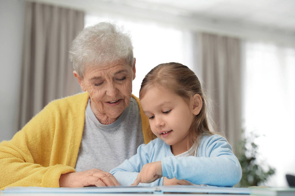 Cute girl and her grandmother reading book at home - Photo, Image
