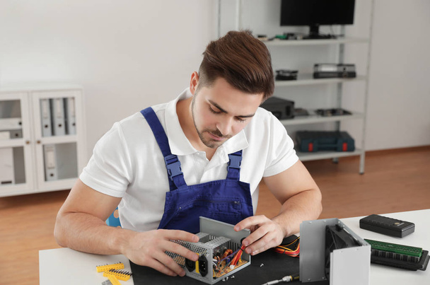 Male technician repairing power supply unit at table indoors - Foto, imagen