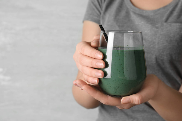 Woman holding glass of spirulina smoothie on grey background, closeup. Space for text - Fotografie, Obrázek