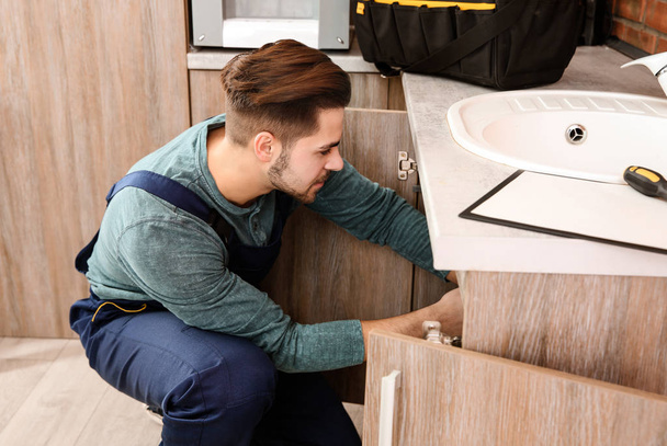 Male plumber in uniform repairing kitchen sink - Foto, Imagem