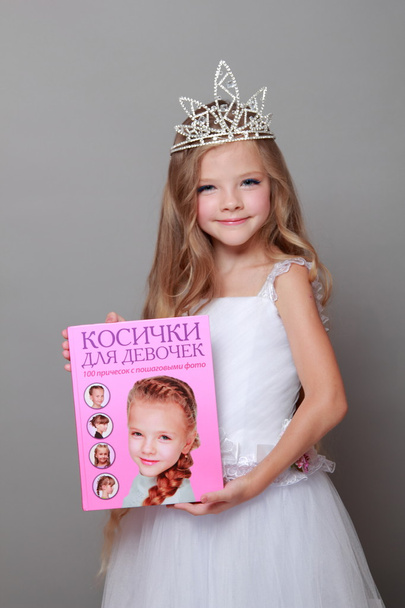 Caucasian little girl with beautiful long hair in the crown and a white dress with a cute smile posing at the camera on a gray background on Beauty and Fashion - Φωτογραφία, εικόνα