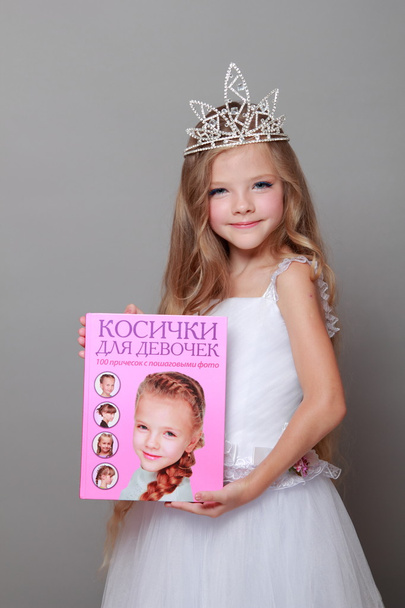 Caucasian little girl with beautiful long hair in the crown and a white dress with a cute smile posing at the camera on a gray background on Beauty and Fashion - Fotó, kép