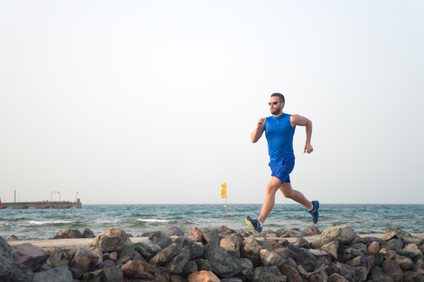 Pain is nothing compared to what it feels like to quit. Running man on beach. Runner training outdoors. Fit male sport fitness exercising in summer. Running sport and hobby. Man fitness coach - Photo, Image