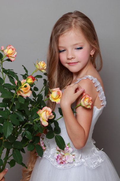 Caucasian girl with beautiful healthy long hairs holding yellow roses with green leaves on a gray background - Valokuva, kuva