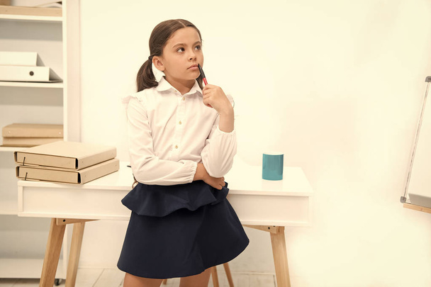 Focused on remembering. Child girl wears school uniform standing with remembering face expression. Schoolgirl smart child looks thoughtful white interior background. Girl try to remember knowledge - Zdjęcie, obraz