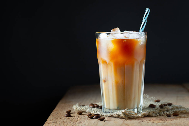 Ledová káva ve vysoké sklenici se smetanou, s ledem a s fazolemi na starém rustikálním dřevěném stole. Studené letní nápoje s trubicemi na černém pozadí s prostorem pro kopírování - Fotografie, Obrázek