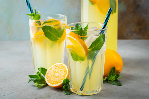 Two glass with lemonade or mojito cocktail with lemon and mint, cold refreshing drink or beverage with ice on rustic blue background - Photo, Image