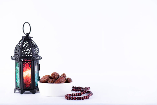 Ramadan Essen und Trinken Konzept. Ramadan Laterne mit arabischer Lampe, Holz Rosenkranz, Tee, Datteln Obst und Beleuchtung auf einem Holztisch auf weißem Hintergrund. - Foto, Bild