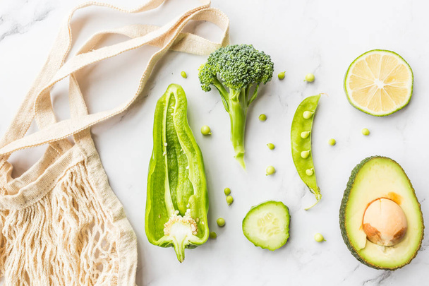Fresh avocado, lime, broccoli, green peas, cucumber, green pepper. Flat lay. Food concept. Green vegetables lying on white marble background - Foto, Bild
