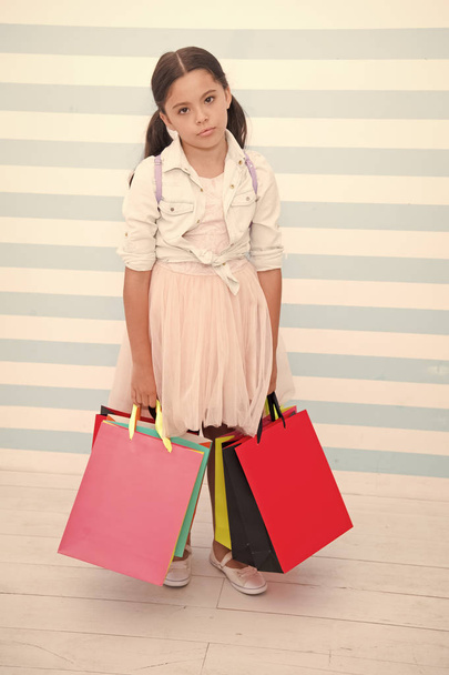 Shopping tiring exhausting activity. Child carries shopping bags striped background. Kid girl spend day buy things supplies for school. Back to school sales season. Girl exhausted holds bags - Photo, Image