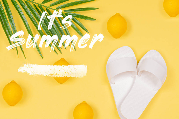 It's Summer text on yellow background with lemon, sandals and green tropical palm leaf. - Foto, immagini