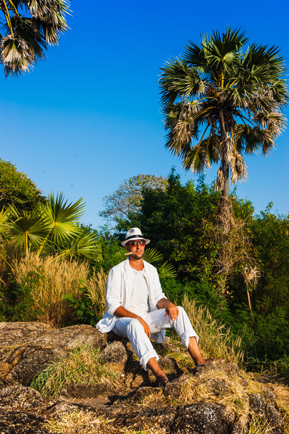 The man in a white suit and hat sitting on a rock on the sea ba - 写真・画像
