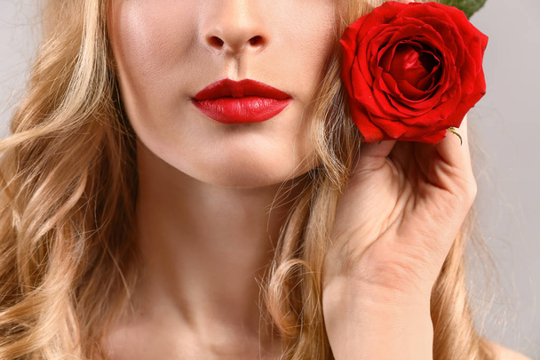 Όμορφη νεαρή γυναίκα με φωτεινό μακιγιάζ και λουλούδι στο φως φόντο, κοντινό πλάνο - Φωτογραφία, εικόνα